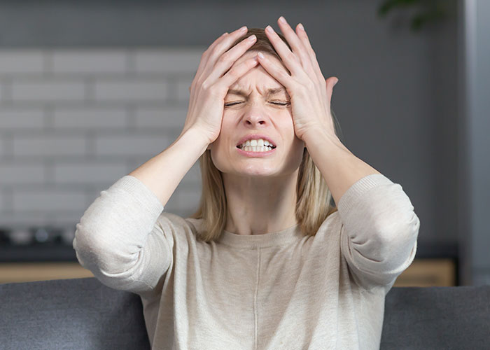 Woman clutching her head in pain on a couch, illustrating warning health signs and severe headache symptoms