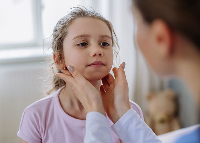 Doctor checking young girl's neck and lymph nodes during pediatric exam, highlighting health signs to watch