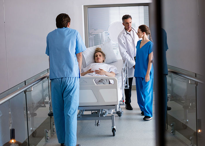 Patient on hospital stretcher with doctor and nurses discussing care, illustrating health signs and concern.