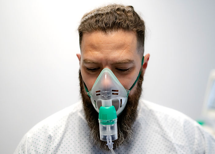 Man in medical gown wearing oxygen mask, illustrating serious health signs and respiratory distress.