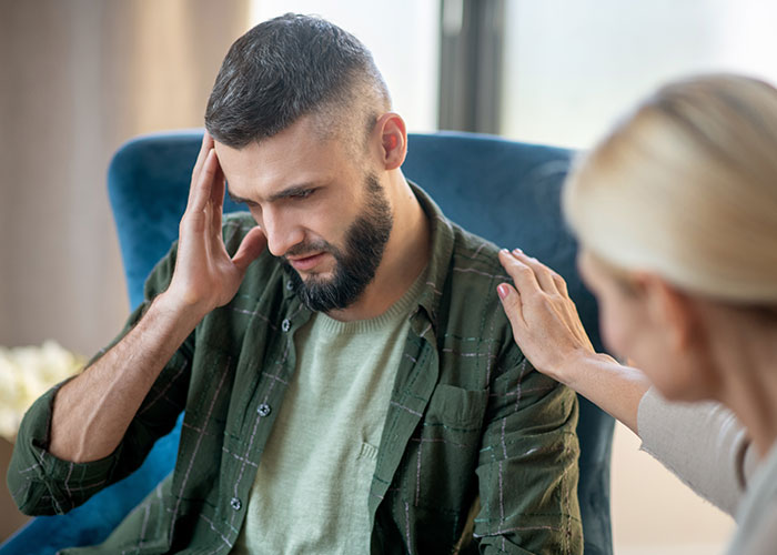 Young man clutching his head while a woman comforts him, illustrating health signs of distress