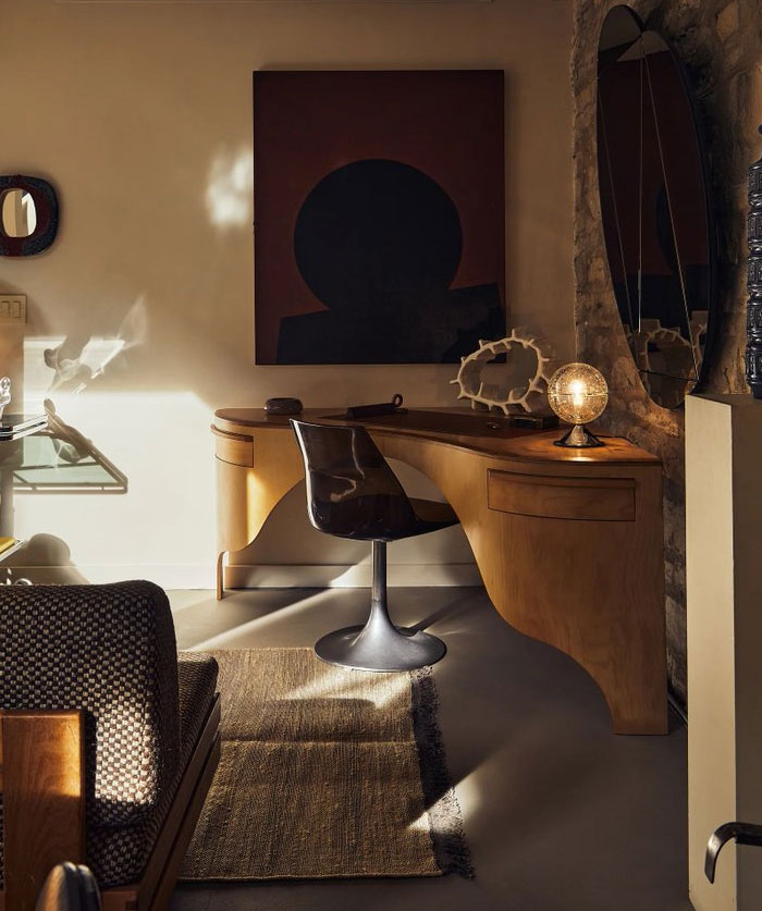 Cozy interior design idea featuring a wooden desk, modern chair, abstract art, and warm ambient lighting in a stylish room.