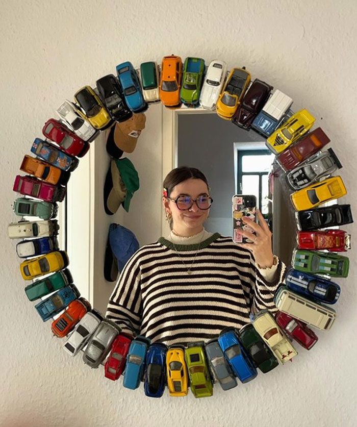 Mirror framed with colorful toy cars reflecting a woman taking a selfie showcasing cool interior design ideas.
