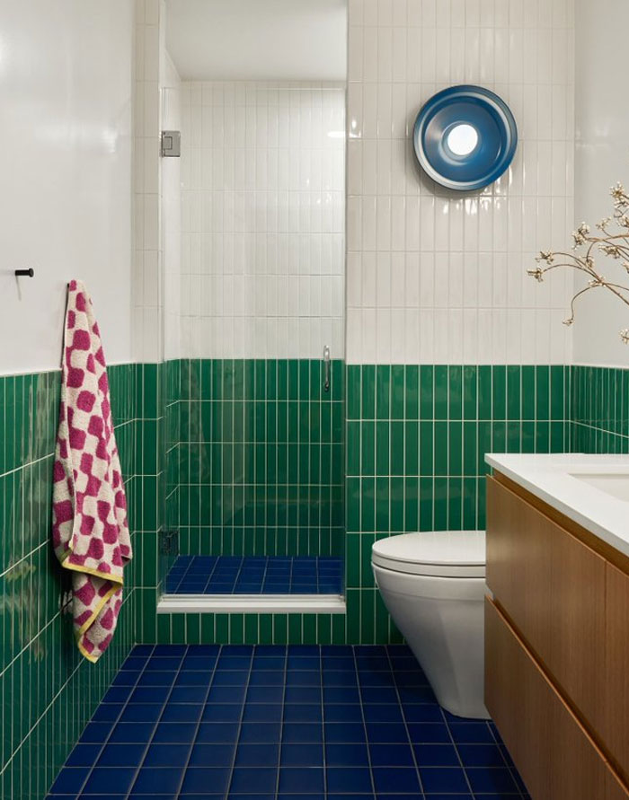Modern bathroom interior design idea featuring green and white tiles, blue floor, and wooden vanity with a sleek toilet.