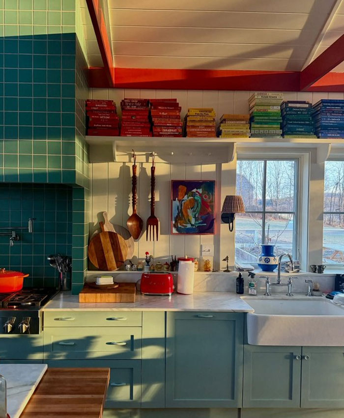 Cozy kitchen with colorful books, teal tiles, pastel cabinets, and eclectic decor showcasing cool interior design ideas.