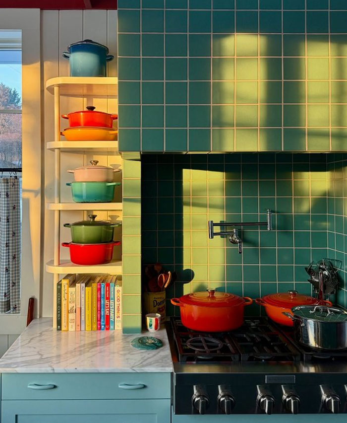 Colorful pots on stove with teal tile backsplash and white shelves filled with cookware and books in stylish interior design.