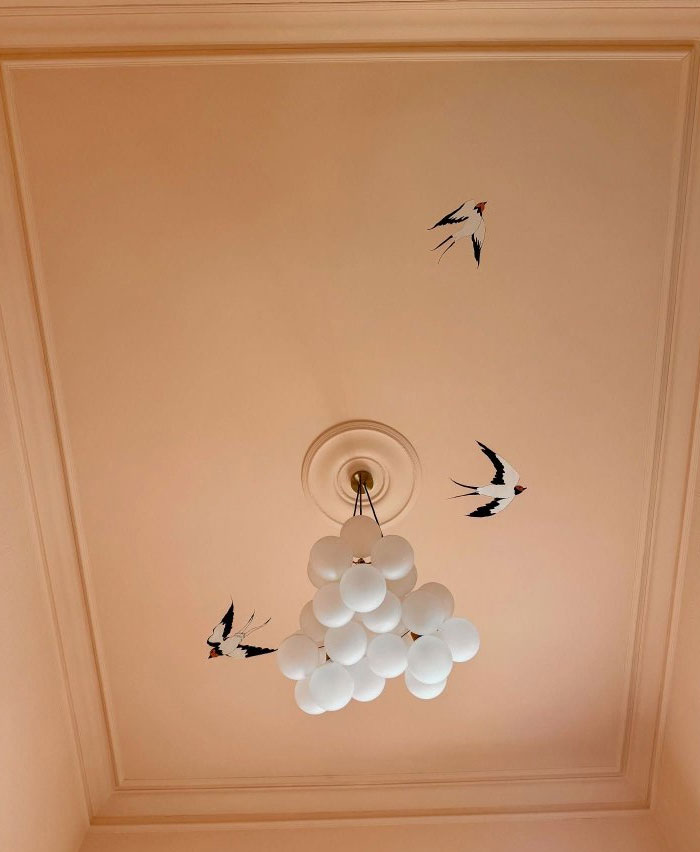 Modern interior design idea featuring a unique cluster chandelier and artistic bird wall decals on a beige ceiling.
