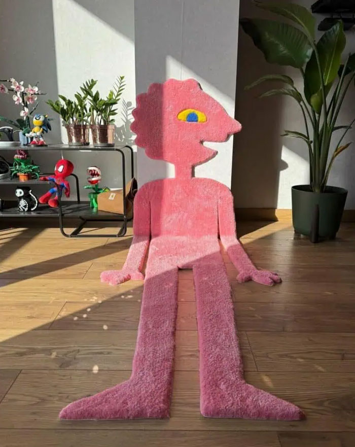 Pink cartoon-shaped rug on wooden floor with plants and decorative items in a modern interior design setting