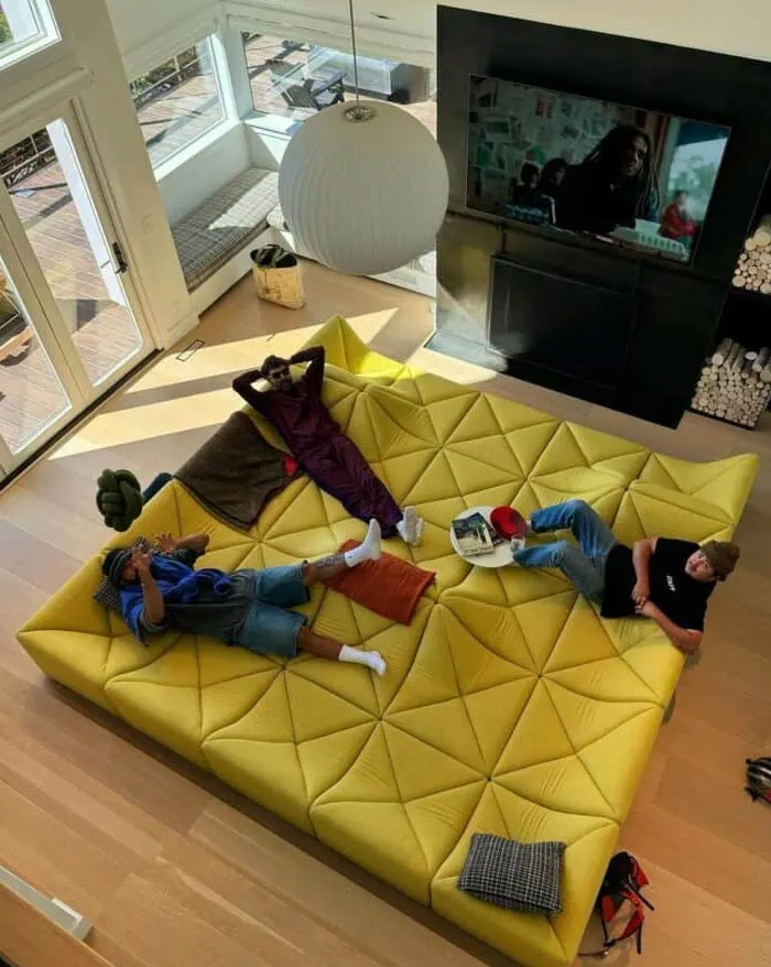 Three people relaxing on a large, modern yellow sofa in a bright living room featuring cool interior design ideas.