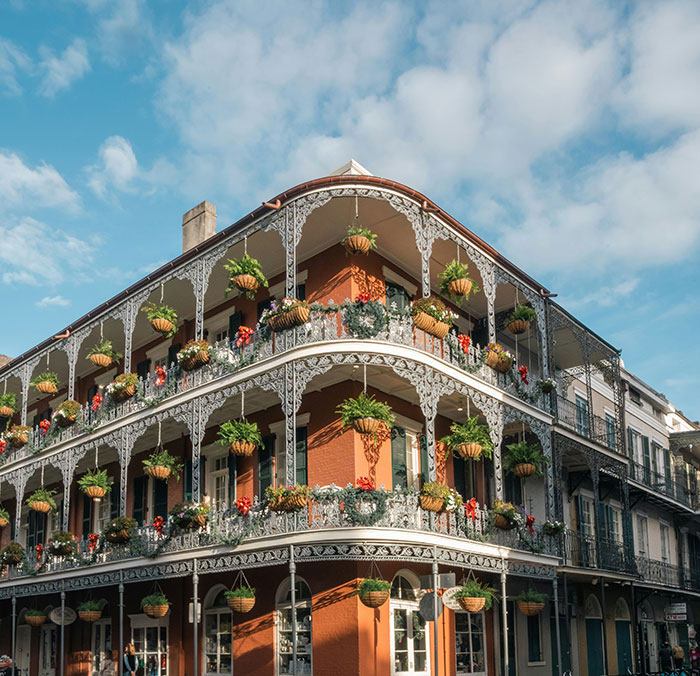 Wrought-iron balconies draped with hanging plants on a sunlit brick corner building, a scene from coolest cities travel