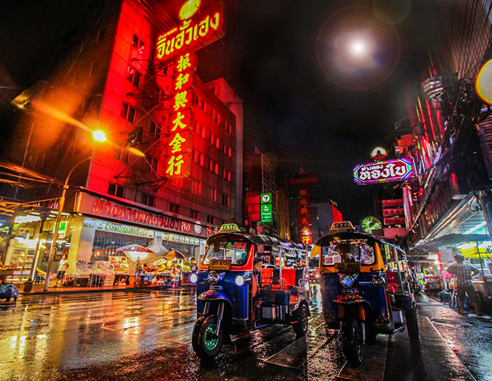 Neon-lit Asian street at night with tuk-tuks on wet pavement, evoking Tokyo and other coolest cities travel scenes