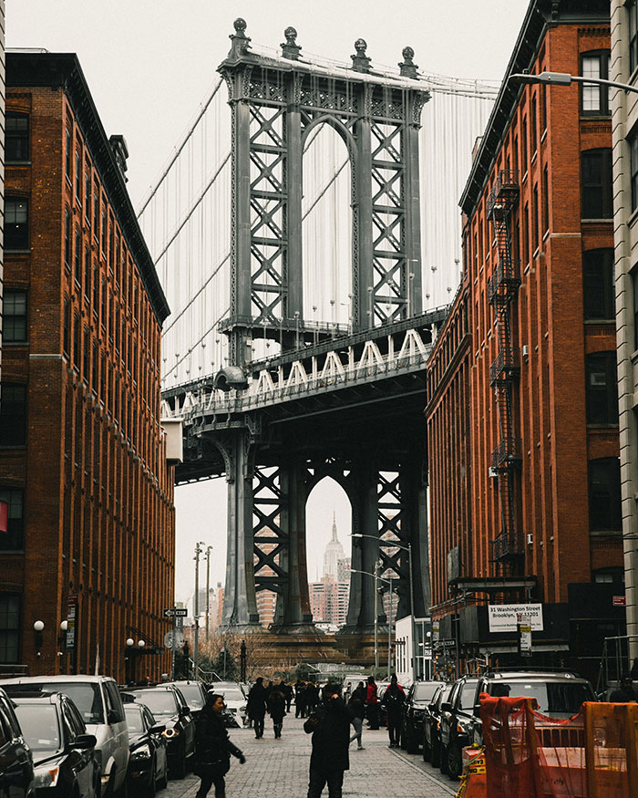Cobblestone street framed by red brick buildings leading to Manhattan Bridge and Empire State, coolest cities photo