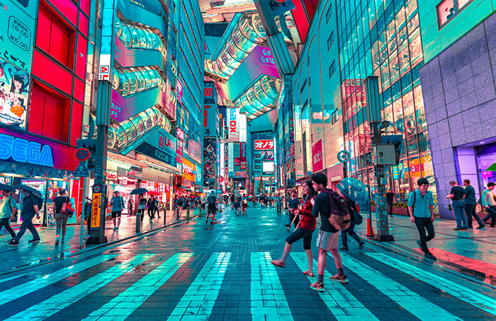 Neon-lit Tokyo street scene with pedestrians crossing a wide zebra crosswalk among shopping arcades at night