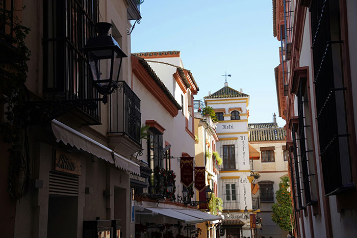 Sunlit narrow European street with white buildings, wrought-iron balconies and cafe awnings, Tokyo