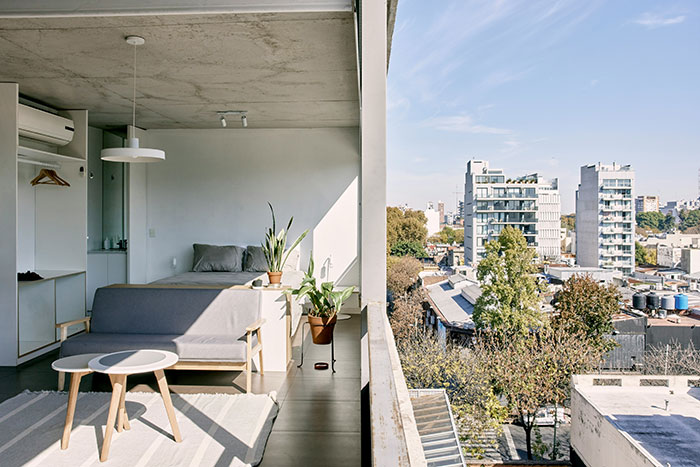 Sunlit modern studio apartment with balcony overlooking Tokyo skyline, minimal decor and potted plants