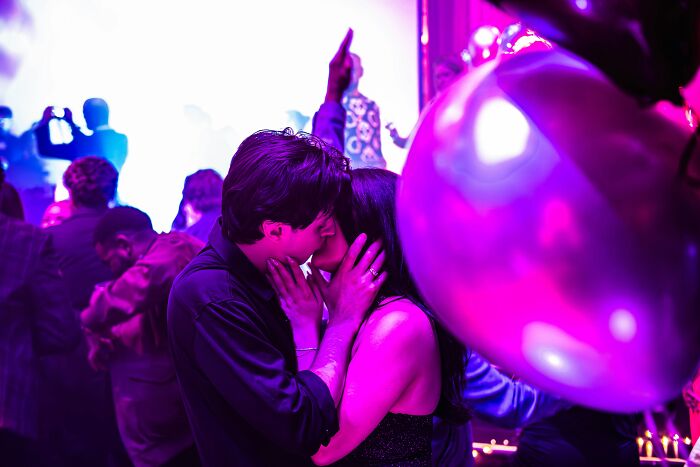 Couple kissing at a nightclub with colorful lights and partygoers dancing, capturing the wild nightclub party atmosphere.