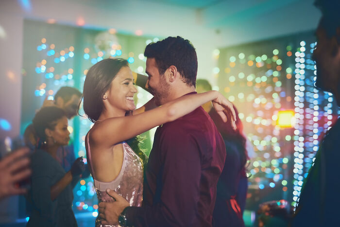 A couple dancing closely at a lively nightclub, surrounded by colorful lights and people enjoying the party atmosphere.
