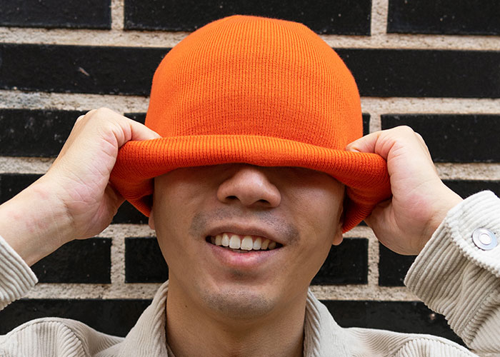 Young man smiling while pulling an orange hat over his eyes, illustrating playful couples house rules taken seriously.