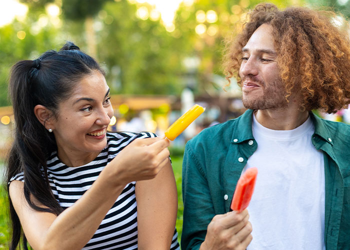 Couple enjoying colorful popsicles outdoors smiling and playfully sharing dumb house rules they now take seriously.