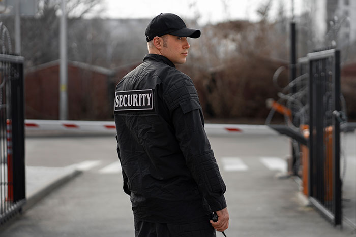 Security guard standing at a gate, representing workplace conflict involving a man reported to HR for inappropriate behavior.