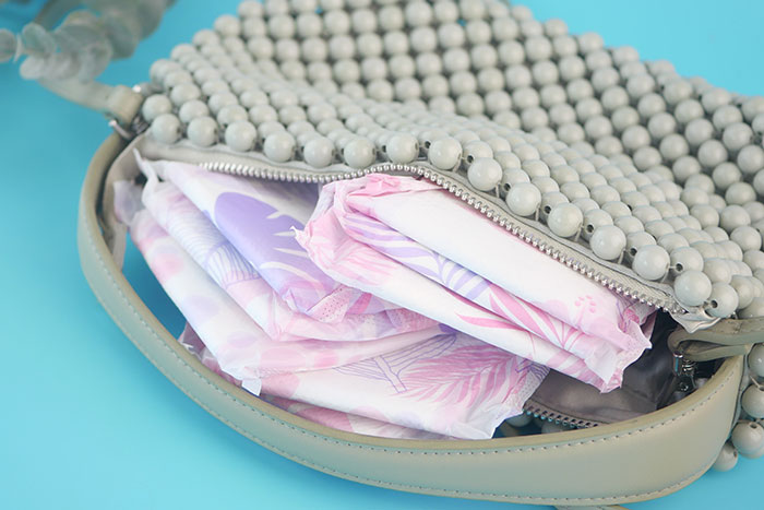 Beaded purse partially unzipped, containing folded feminine hygiene pads on a blue background representing workplace issues.