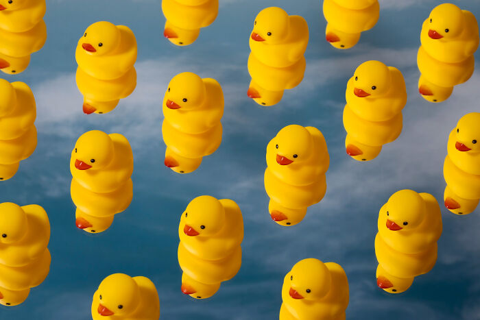 Pattern of yellow rubber ducks floating against a blue cloudy sky, playful background for high school secrets feature