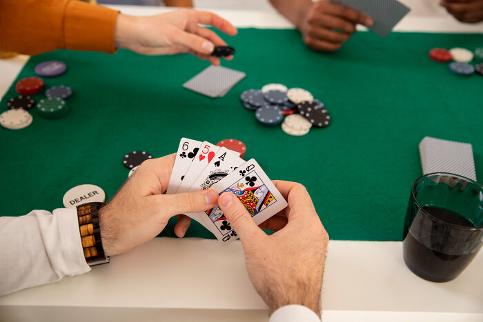 Hands holding playing cards at poker table with chips and dealer button, high school secrets theme