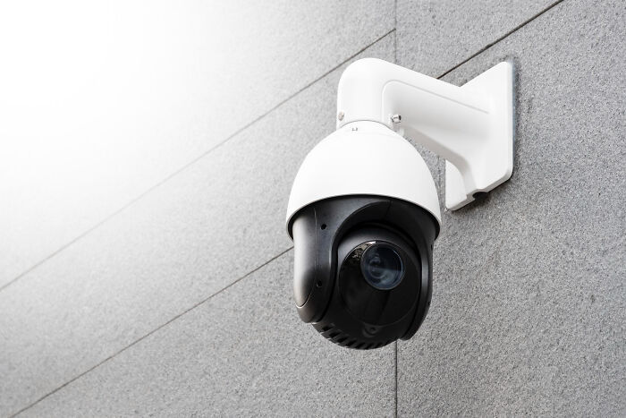 Surveillance camera on a gray wall, symbolizing high school secrets being observed and revealed later