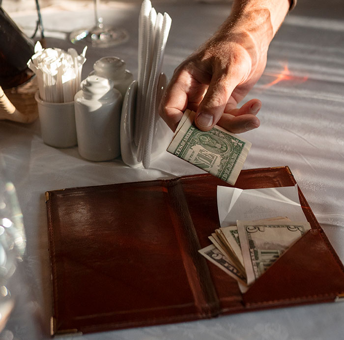 Hand placing a dollar bill into a leather wallet on a table, illustrating sharp intelligence in a financial context.
