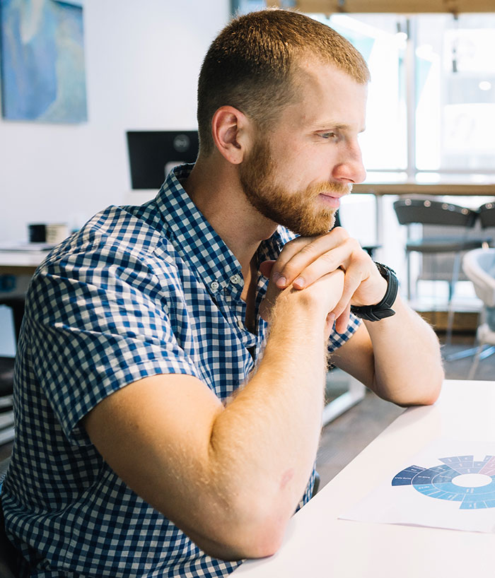 Young man in a checkered shirt thoughtfully analyzing a chart, showcasing sharp intelligence in a modern office setting.