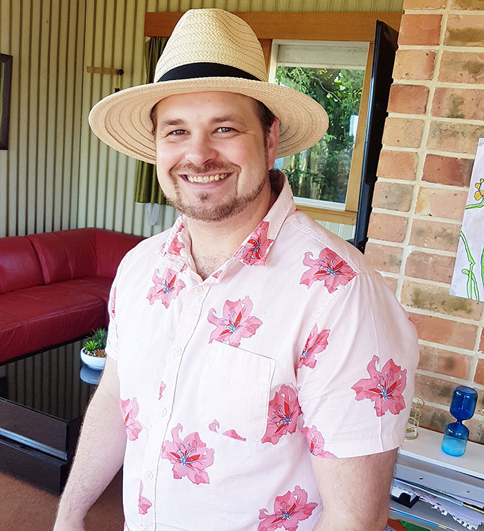 Man smiling indoors wearing a pink floral shirt and straw hat, showcasing intelligence so sharp it almost feels like brain spaghetti.