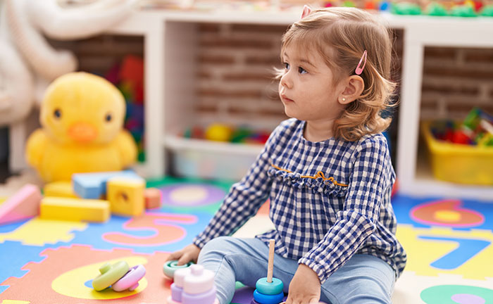 Toddler girl with sharp intelligence playing with educational toys on colorful foam numbers mat indoors.