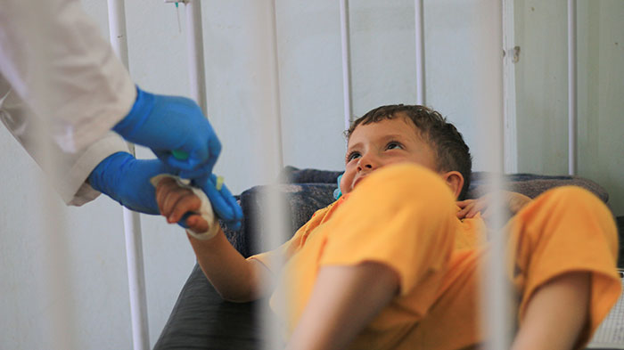 Child in hospital bed holding hands with a medical professional wearing gloves, showcasing sharp intelligence and trust.