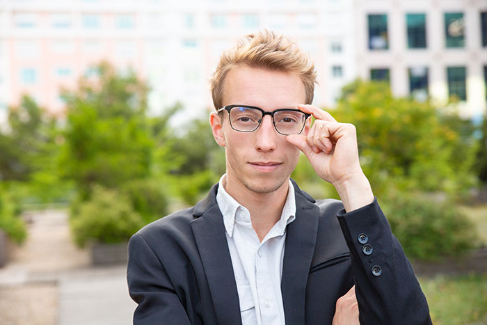 Young man wearing glasses and a blazer outdoors, representing intelligence so sharp it made me feel like brain was spaghetti.