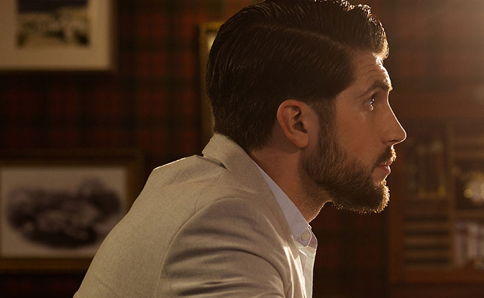 Man with sharp intelligence deep in thought, side profile showing focused expression in warm, cozy indoor setting.