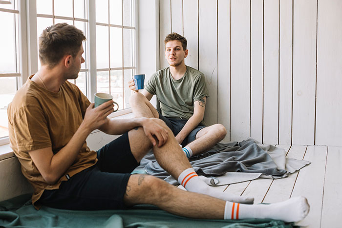 Two young men sitting by a window, drinking coffee and having a sharp intelligence conversation in a relaxed setting.