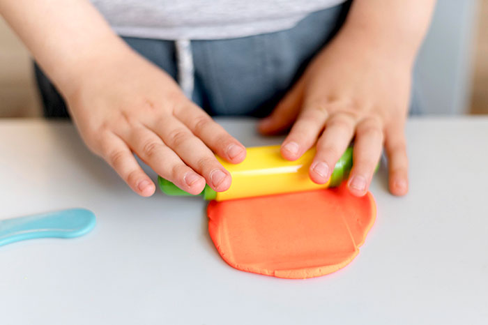 Child using a rolling pin to flatten orange playdough, illustrating creativity and sharp intelligence in early learning.