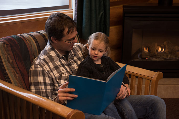 Man and child reading a book together by the fireplace, illustrating sharp intelligence and thoughtful learning.