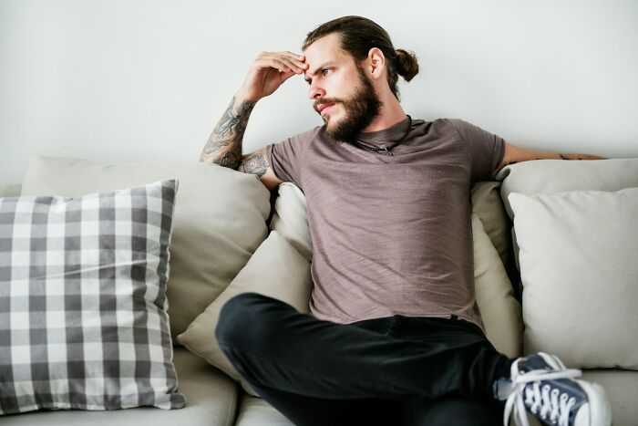 Man with tattoos sitting on a couch looking thoughtful, capturing the shock of people after they got out of prison.