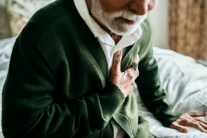 Elderly man clutching chest in pain at home, illustrating unethical doctor behavior with patient concerns.