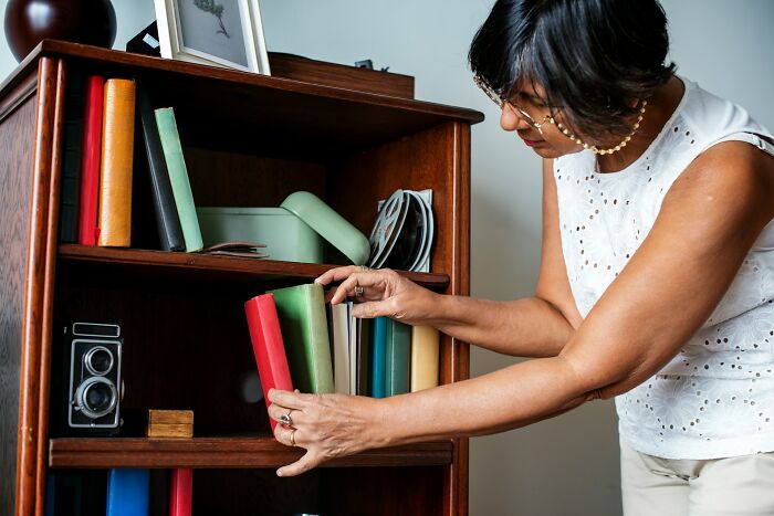 Woman organizing books on a wooden shelf, illustrating unusual teacher behavior witnessed in class moments.