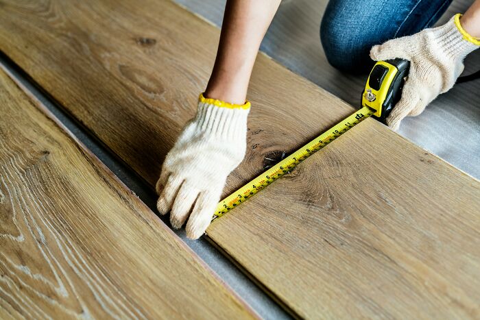 Person wearing gloves measuring wood floor planks with tape measure in moments so ridiculous people thought they were being pranked