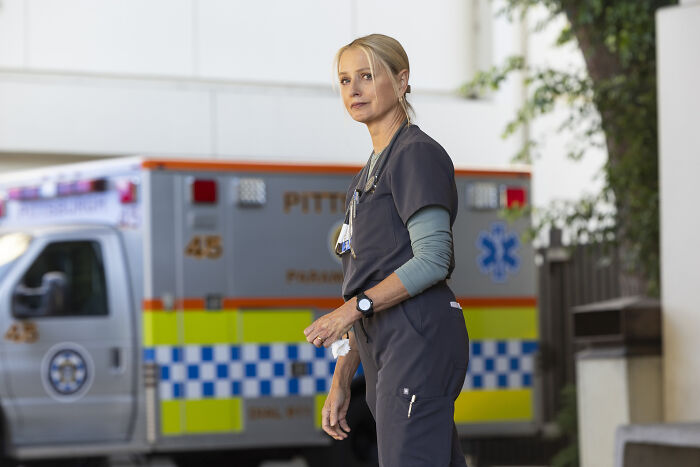 Katherine LaNasa as Nurse Dana in dark scrubs standing near an ambulance in a hospital setting. Katherine LaNasa as Nurse Dana in dark scrubs standing near an ambulance in a hospital setting.