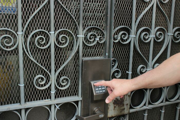 Person pressing keypad on secure metal gate lock, illustrating safety measures women use while living alone. Person pressing keypad on secure metal gate lock, illustrating safety measures women use while living alone.