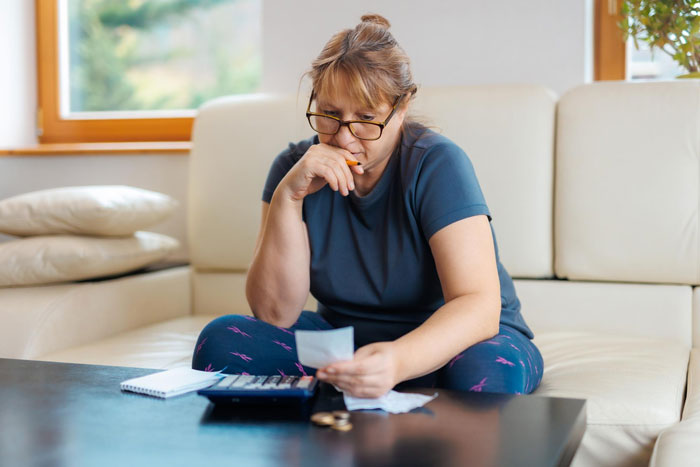 Woman sitting on couch, focused on bills and calculator, representing daughter step up to help mom with finances.