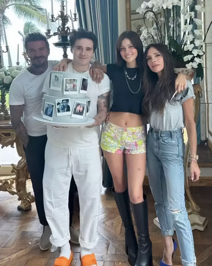 David Beckham and family posing indoors with son holding a photo-decorated cake during ongoing family rift crisis.