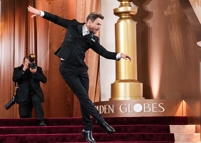 Man in a black tuxedo losing balance on red carpet steps at the 2026 Golden Globes awkward moment captured by photographer.