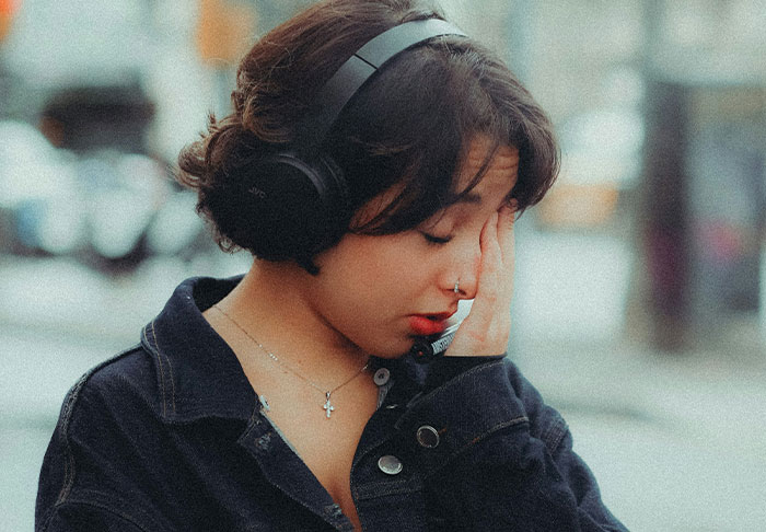 Woman upset and frustrated after unexpected walking trip while managing diabetes, wearing headphones and dark jacket outdoors.