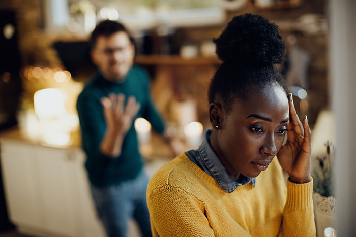 Distressed mom regrets becoming a parent, looking stuck while husband argues in the background.