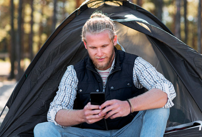 Man sitting outside a tent using his phone, hinting at a camping trip with his brother but the brother was at home. Man sitting outside a tent using his phone, hinting at a camping trip with his brother but the brother was at home.